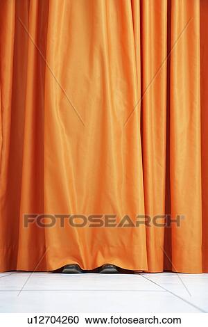 Stock Image - Person hiding behind orange curtain. Fotosearch