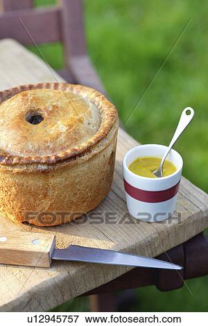 Pork pie knife and cup of mustard on table outdoors View Large Photo Image Stock Photo - Pork pie knife and cup of mustard on table outdoors. Fotosearch