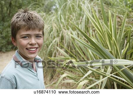 Portrait of boy (10-12) standing by outdoor plant smiling View Large Photo Image Stock Image - Portrait of boy (10-12) standing by outdoor plant smiling. Fotosearch