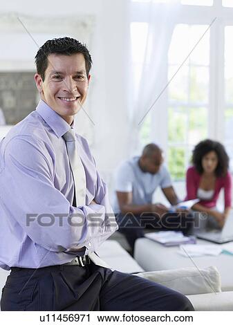 Portrait of business man in living room couple sitting in background View Large Photo Image Stock Image - Portrait of business man in living room couple sitting in background. Fotosearch