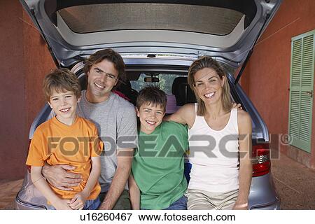 Stock Photo - Portrait of family with two sons (6-11) sitting on car tailgate. Fotosearch