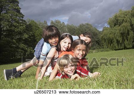 Stock Image - Portrait of five children (7-9) lying on top of each other in meadow. Fotosearch