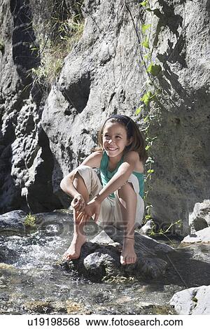Portrait of girl (10-12) sitting on rock by stream smiling View Large Photo Image Stock Photo - Portrait of girl (10-12) sitting on rock by stream smiling. Fotosearch