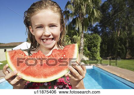 Stock Photograph - Portrait of girl (5-6) eating watermelon by swimming pool. Fotosearch