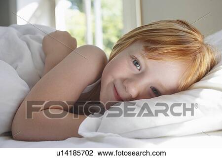 Stock Image - Portrait of girl (5-6) lying in bed smiling. Fotosearch