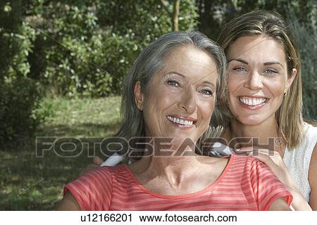 Stock Image - Portrait of mother with adult daughter in garden smiling close-up. Fotosearch