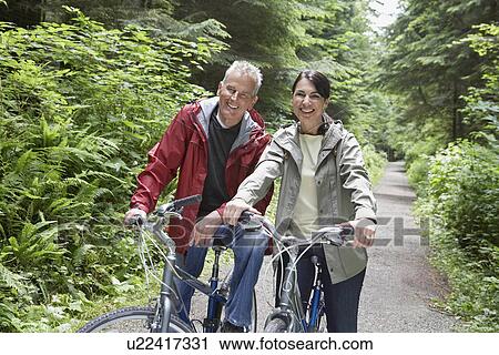 Portrait of senior man and middle-aged woman on bicycles in forest smiling View Large Photo Image Stock Image - Portrait of senior man and middle-aged woman on bicycles in forest smiling. Fotosearch