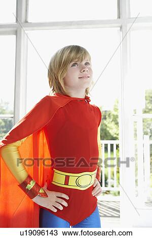 Stock Image - Portrait of young boy (7-9) in superhero costume hands on hip indoors. Fotosearch