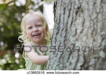 Portrait of young girl (1-2) peeking from behind tree laughing View Large Photo Image Stock Photograph - Portrait of young girl (1-2) peeking from behind tree laughing. Fotosearch