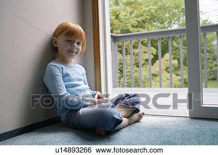 Stock Photograph - Portrait of young girl (5-6) sitting cross-legged on carpet. Fotosearch