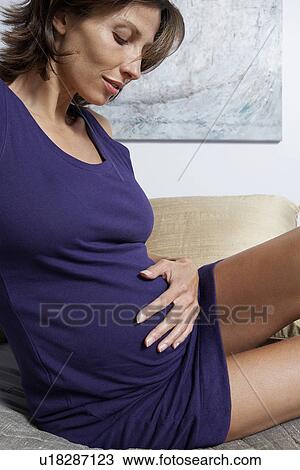 Stock Image - Pregnant woman holding stomach on bed in bedroom. Fotosearch