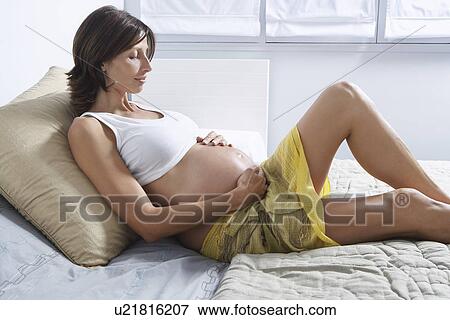 Pregnant woman holding stomach on bed in bedroom View Large Photo Image Stock Photo - Pregnant woman holding stomach on bed in bedroom. Fotosearch