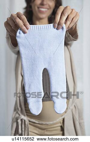 Pregnant woman holding up baby pants indoors View Large Photo Image Stock Image - Pregnant woman holding up baby pants indoors. Fotosearch