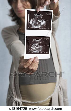 Pregnant woman holding up sonogram indoors View Large Photo Image Stock Photo - Pregnant woman holding up sonogram indoors. Fotosearch