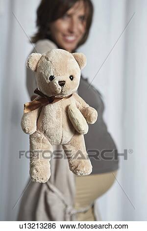 Pregnant woman holding up teddy bear indoors View Large Photo Image Stock Photograph - Pregnant woman holding up teddy bear indoors. Fotosearch