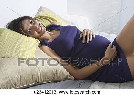 Pregnant woman lying in bed smiling in bedroom View Large Photo Image Stock Image - Pregnant woman lying in bed smiling in bedroom. Fotosearch