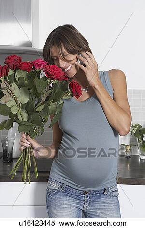 Pregnant woman using mobile phone while holding roses in kitchen View Large Photo Image Stock Photography - Pregnant woman using mobile phone while holding roses in kitchen. Fotosearch