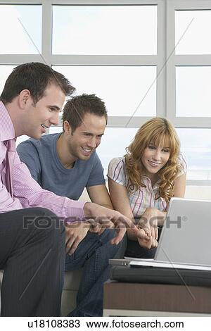 Stock Image - Real estate agent using laptop with couple in new home. Fotosearch