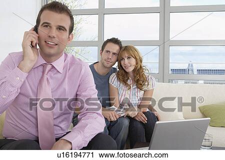 Stock Image - Real estate agent using mobile phone with couple in new home. Fotosearch