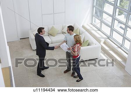 Real estate agent with couple in new home man shaking hand elevated view View Large Photo Image Picture - Real estate agent with couple in new home man shaking hand elevated view. Fotosearch
