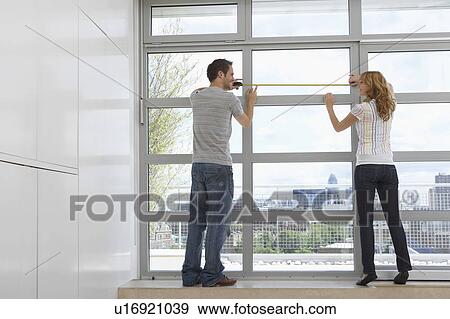 Stock Photo - Rear view of young couple measuring window in modern apartment. Fotosearch