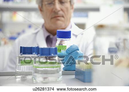 Picture - Scientist looking at specimen bottle in laboratory focus on bottle. Fotosearch