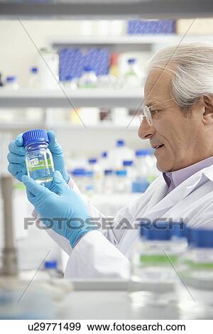 Stock Photo - Scientist looking at specimen bottle in laboratory. Fotosearch