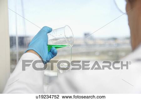 Stock Image - Scientist pouring green liquid in laboratory focus on hand and beaker. Fotosearch