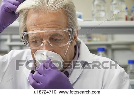 Stock Image - Scientist putting on safety mask in laboratory. Fotosearch