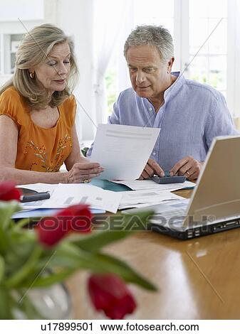 Senior couple looking at bills sitting at dining table View Large Photo Image Stock Image - Senior couple looking at bills sitting at dining table. Fotosearch