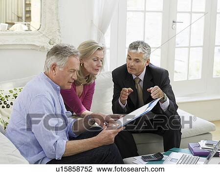 Stock Image - Senior couple sitting on sofa with financial advisor elevated view. Fotosearch