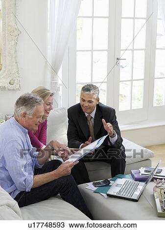 Stock Image - Senior couple sitting on sofa with financial advisor elevated view. Fotosearch