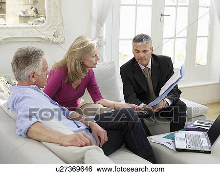 Stock Photograph - Senior couple sitting on sofa with financial advisor elevated view. Fotosearch