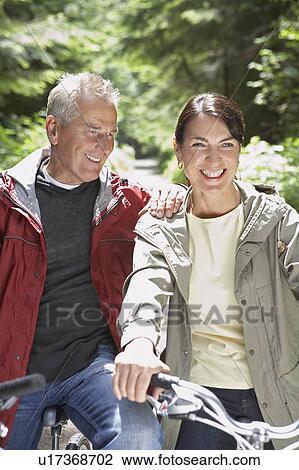 Stock Image - Senior man and middle-aged woman on bikes in forest laughing. Fotosearch
