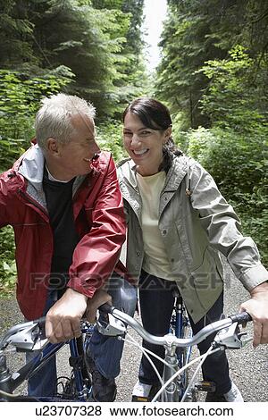 Senior man and middle-aged woman on bikes in forest laughing View Large Photo Image Stock Photo - Senior man and middle-aged woman on bikes in forest laughing. Fotosearch