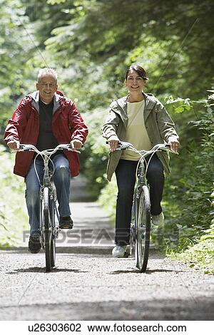 Stock Image - Senior man and middle-aged woman riding bicycles in forest front view. Fotosearch