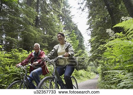 Senior man and middle-aged woman riding bicycles in forest smiling View Large Photo Image Stock Image - Senior man and middle-aged woman riding bicycles in forest smiling. Fotosearch