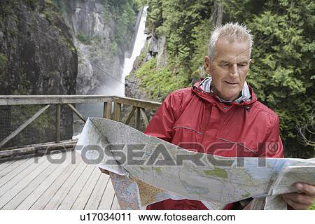 Stock Image - Senior man reading map waterfall in background. Fotosearch