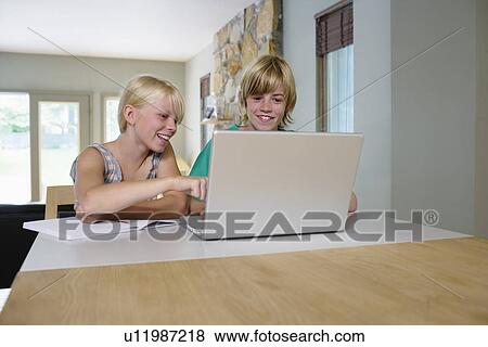Sister and brother (8-11) sitting at table using laptop smiling View Large Photo Image Stock Photo - Sister and brother (8-11) sitting at table using laptop smiling. Fotosearch