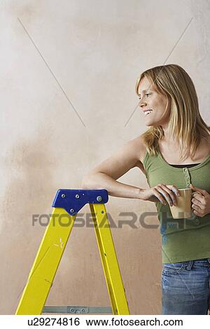 Smiling woman leaning on step ladder holding mug View Large Photo Image Stock Photograph - Smiling woman leaning on step ladder holding mug. Fotosearch