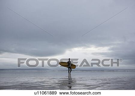 Surfer carrying surfboard on beach back view View Large Photo Image Stock Photo - Surfer carrying surfboard on beach back view. Fotosearch