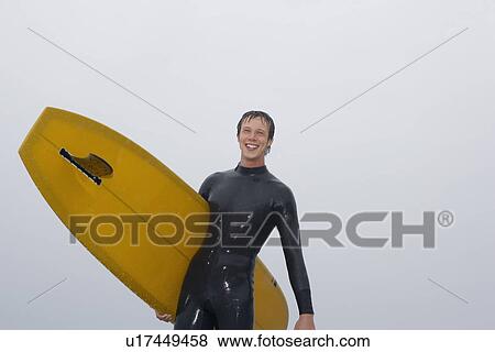 Surfer carrying surfboard on beach low angle view portrait View Large Photo Image Stock Photo - Surfer carrying surfboard on beach low angle view portrait. Fotosearch