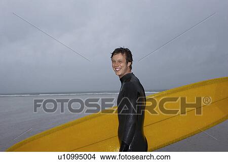 Surfer carrying surfboard on beach portrait side view View Large Photo Image Picture - Surfer carrying surfboard on beach portrait side view. Fotosearch