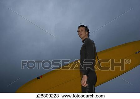 Surfer carrying surfboard on beach side view low angle view View Large Photo Image Stock Image - Surfer carrying surfboard on beach side view low angle view. Fotosearch