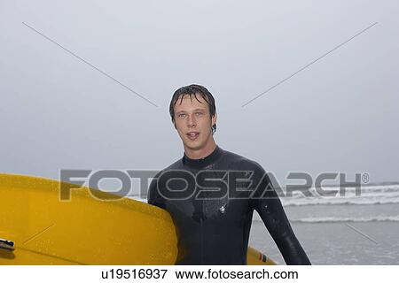 Stock Photo - Surfer carrying surfboard on beach. Fotosearch