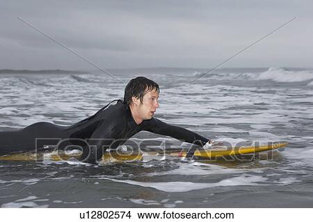Picture - Surfer puddling on surfboard in water side view. Fotosearch