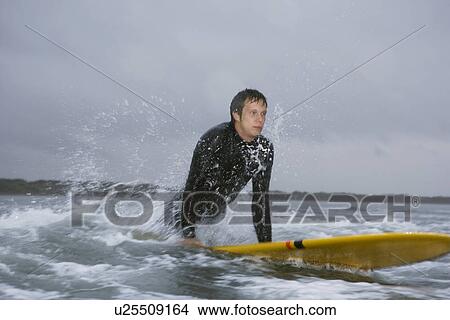 Surfer pulling himself up onto surfboard in water View Large Photo Image Picture - Surfer pulling himself up onto surfboard in water. Fotosearch