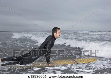 Surfer pulling himself up onto surfboard in water side view View Large Photo Image Stock Photography - Surfer pulling himself up onto surfboard in water side view. Fotosearch