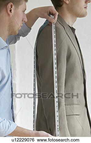 Stock Photograph - Tailor measuring jacket sleeve on man side view close up. Fotosearch