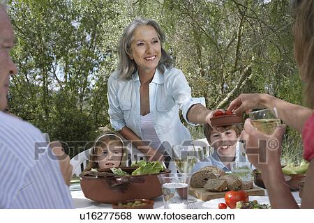 Stock Photo - Three-generation family including two children (5-6) eating at garden table. Fotosearch